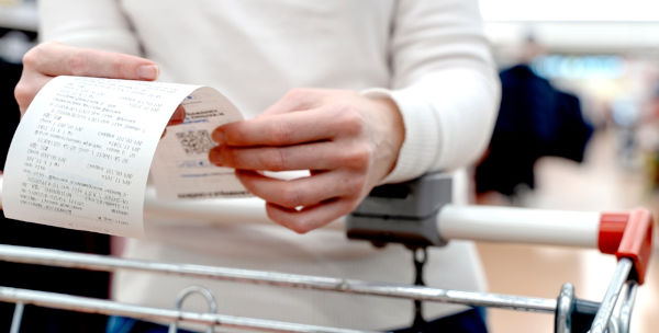 Pessoa segurando nota fiscal do supermercado na qual podem ser vistos os impostos, tais como o ICMS.